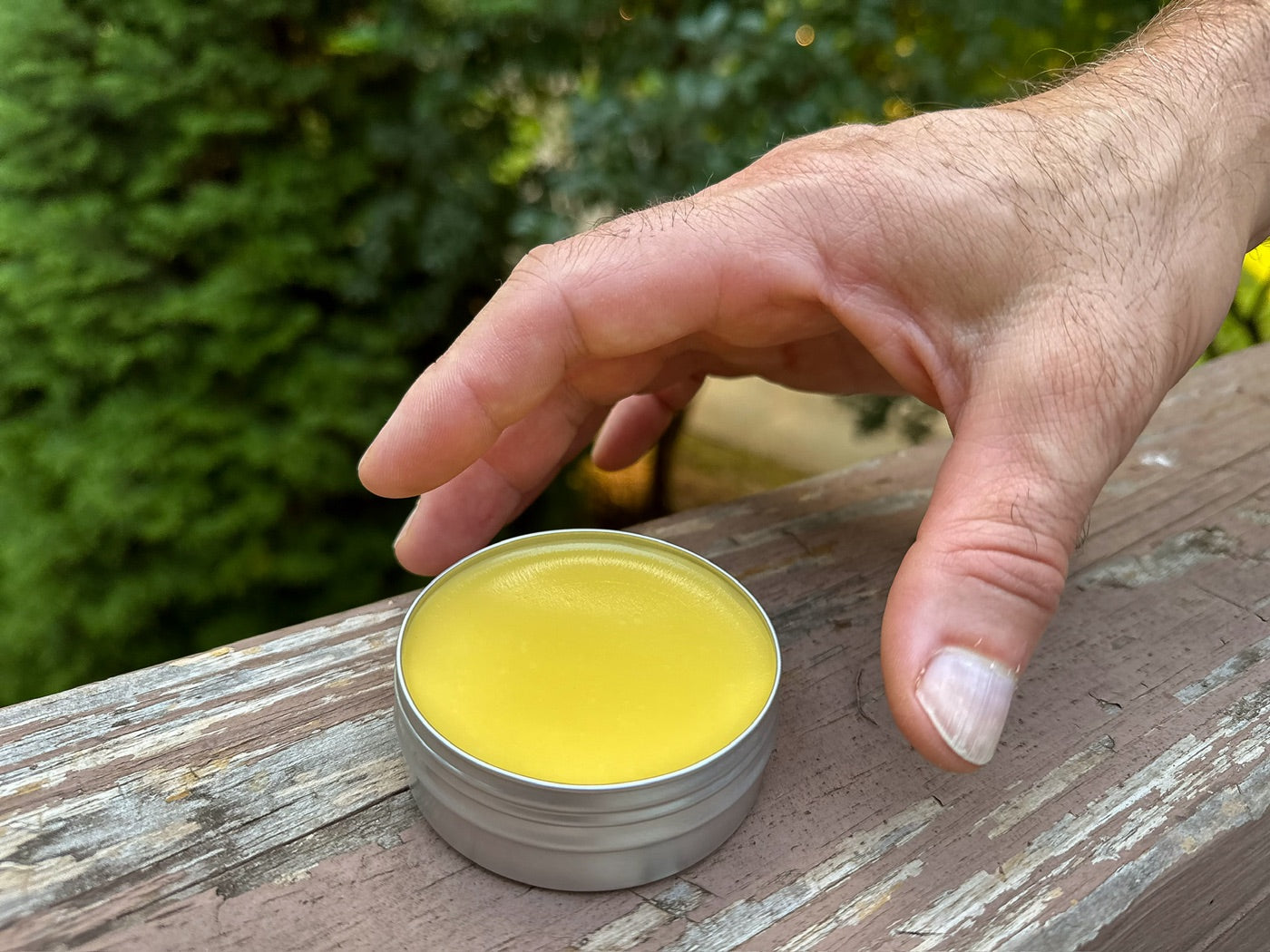 A hand reaching for an open tin of Soothe Salve on a weathered railing