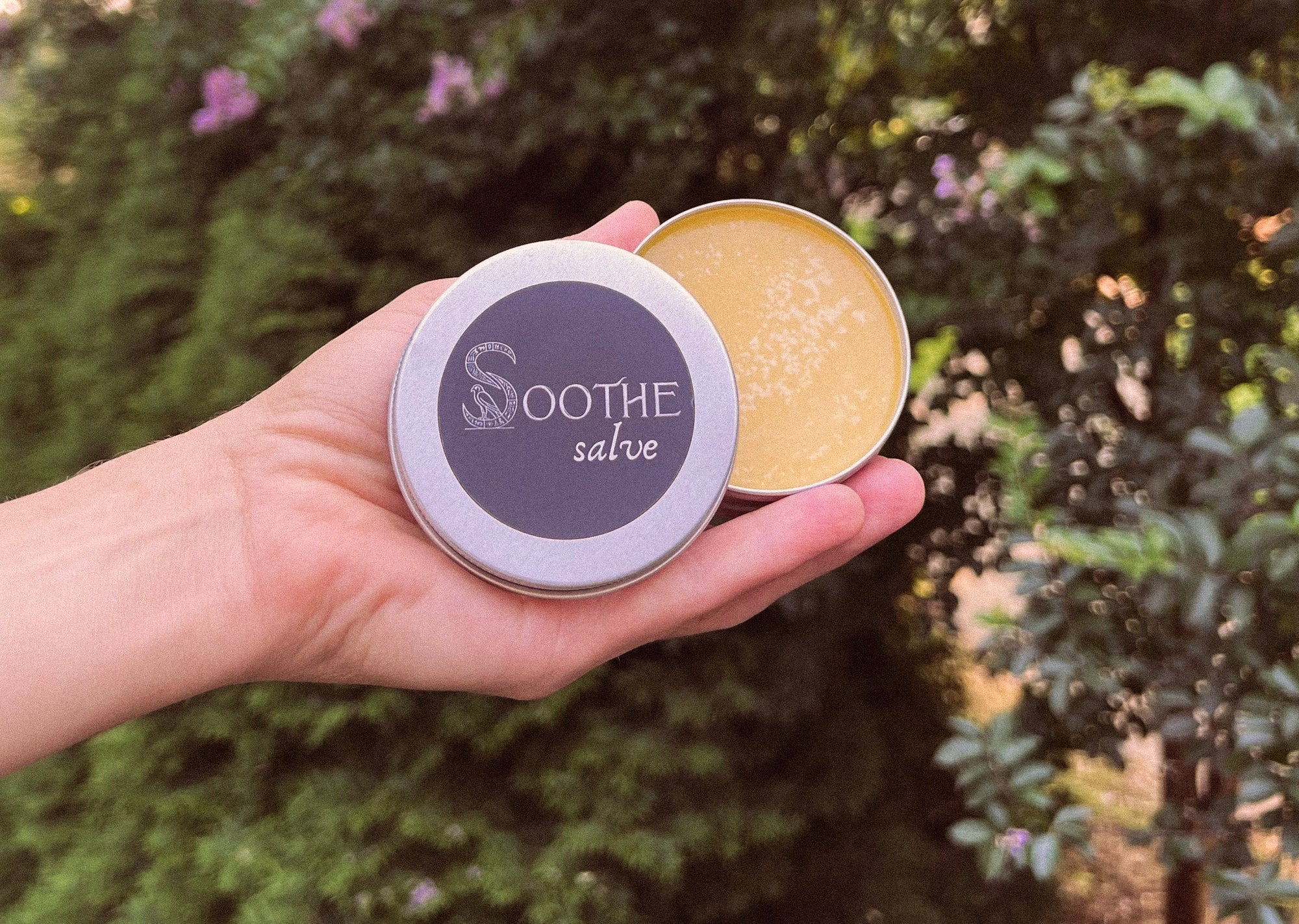 A hand holding an open tin of Soothe Salve outdoors
